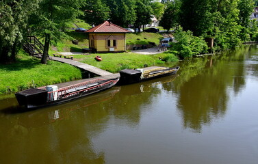 A view of several barges, boats, or other vessels parked next to some wooden piers or marinas next to a vast yet shallow lake or river seen on a sunny summer day on a Polish countryside during a hike