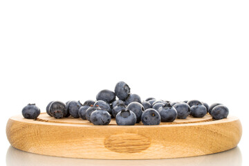 Several berries of ripe dark purple blueberries on a round tray made of wood, close-up, isolated on white.