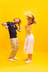 Portrait of young man and woman dancing, posing isolated over yellow studio background. Party time. Looking happy.