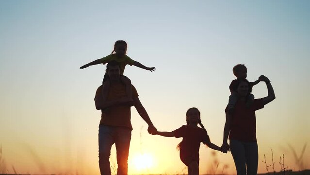 people in the park. happy family silhouette fun walk at sunset. mom dad and daughters walk holding hands in park. happy family kid dream concept. parents and kids walking back silhouette. join family