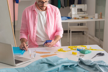 clothing designer sitting in his studio, sewing workshop. holding mobile, phone, smartphone
