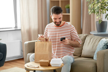 communication, leisure and people concept - man using smartphone for takeaway food order check up at home