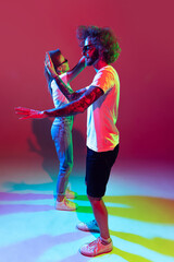 Fototapeta premium Portrait of young stylish man and woman dancing, posing isolated over red background in neon light. Contemp dancers