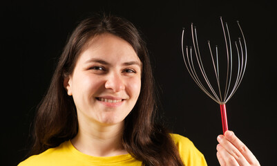 A woman with a metal flexible massager for self-massage of the head on a black background.