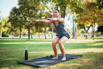 Asian sporty girl working out outdoors in the park. She is doing squat exercises on a mat.