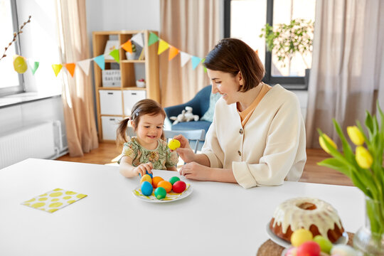 holidays, family and people concept - happy mother and little baby daughter with colored easter eggs at home
