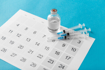 Fototapeta na wymiar medicine, vaccination and healthcare concept - disposable syringe and calendar on blue background