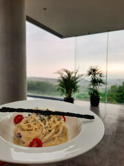 A carbonara spaghettis with a beautiful landscape view in the background served in a white plate.  