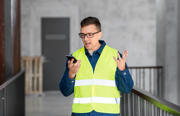 architecture, construction business and building concept - angry male architect in safety west calling on smartphone or using voice command recorder at office