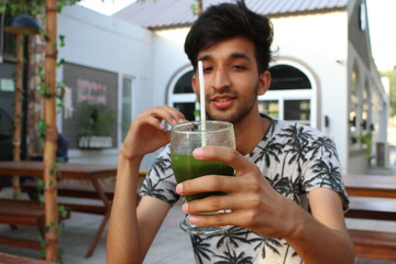 Young man sitting in a restaurant outdoor sitting place enjoying mint margarita in hot weather