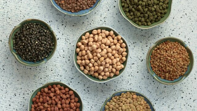 Dry chickpeas, black chickpeas, black gram, brown lentils, green chickpeas, green lentils and horse gram in bowls. Legumes assortment, table spin.