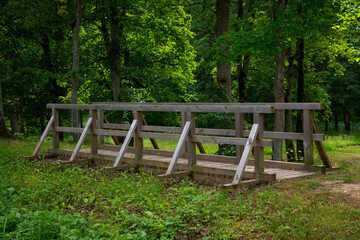 wooden bridge in the park on a tourist path with green leaves of trees in summer that leads over the river channel.