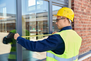 construction business and building concept - male builder with ruler measuring window