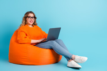 Photo full body view of woman typing on laptop sitting in armchair isolated on turquoise colored background