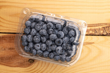 Organic blueberries in a plastic container, close-up, on a wooden table, top view.