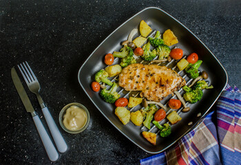 Grilled chicken breast steak with potatoes, cherry tomatoes, broccoli and sauce in pan ready to serve, top view.
