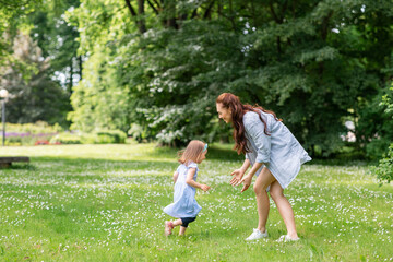 Naklejka na ściany i meble family, motherhood and people concept - happy mother with little daughter playing at summer park or garden