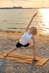 fitness, sport, and healthy lifestyle concept - woman doing yoga triangle pose on beach over sunset