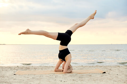 fitness, sport, and healthy lifestyle concept - woman doing yoga headstand on beach over sunset
