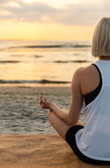 Fototapeta na wymiar yoga, mindfulness and meditation concept - woman meditating in lotus pose on beach over sunset