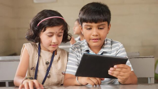 Two Elementary Students Busy Reading From Digital Tablet At Classroom - Concept Of Technology, E-learning And Development