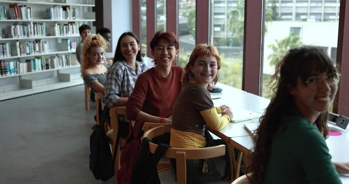 Multiracial young students learing together inside school library while smiling on camera