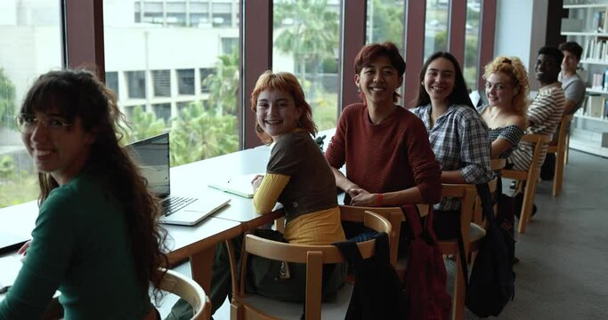 Multiracial young students learing together inside school library while smiling on camera
