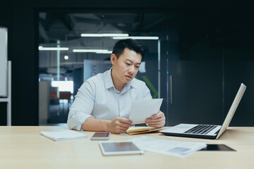 Sad over thinking asian businessman reading bad news letter from bank, male boss in shirt working in office