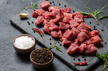 Diced cubed beef meat on stone board with thyme and peppers