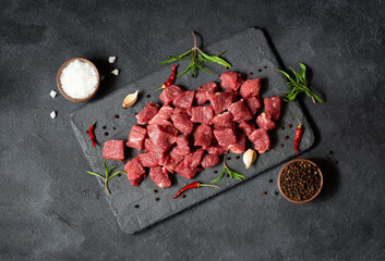 Diced cubed beef meat on stone board with thyme and peppers - obrazy, fototapety, plakaty