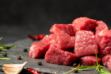 Diced cubed beef meat on stone board with thyme and peppers