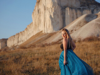 Fashionable woman on desert field near mountain wearing black top and blue tulle skirt - 516760952