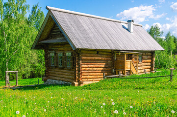 Obraz premium Large diameter logs and windows in a rustic log house built in the 19th century. Dark log walls of the house. Rustic architecture. A house in the village on a background of green grass and blue sky.