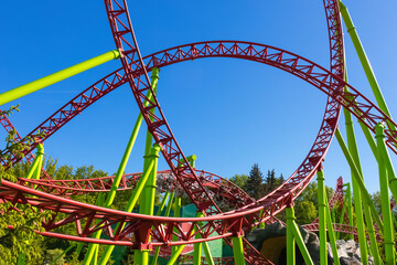 Roller coaster with speeding trolleys against green trees and blue sky