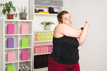 Young obese woman warming up in yoga studio. Obese Caucasian female with short green hair exercising in order to lose some weight