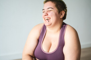 Beautiful energetic young plus size woman in sports bra having a big smile and looking happy. Dyed hair overweight female laughing while workout.