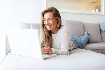 Communication is very important. Top view portrait of young smiling woman sitting on sofa at home with laptop laying on back-rest. Business woman working from home