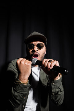 emotional middle east hip hop performer with clenched fist singing in microphone on black.