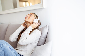 Portrait of a beautiful young woman lying on sofa with headphones on and closed eyes, relaxing. Good music finds it's way to your heart. Woman using a smartphone and headphones on the sofa at home