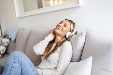 Pleased young woman in headphones listening to music while relaxing on sofa at home. Shot of a young woman using headphones while relaxing on the sofa at home