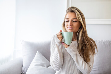 Portrait of joyful young woman enjoying a cup of coffee at home. Smiling pretty girl drinking hot...