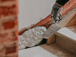 A hand in a construction glove of a plasterer guy throws putty on a hole in the wall of the landin