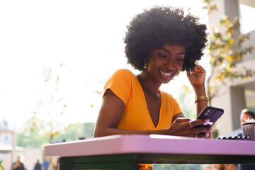 Happy afro woman using mobile phone at outdoor cafe