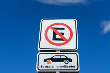 Parking ban sign with Spanish-language wheel block, against blue sky