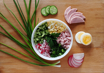 Salad with greens, ham, egg and vegetables in a white plate on a wooden background.