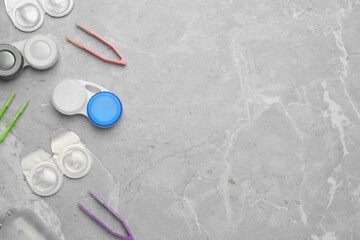 Packages with contact lenses, cases and tweezers on light grey marble table, flat lay. Space for text