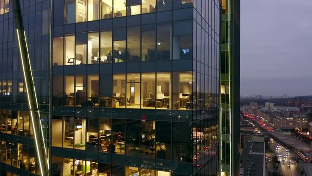 Drone shot of an office building in the late evening with interior lights on and people working inside the night skyscraper. Office windows in Skyscrapers City International Business Center at night.