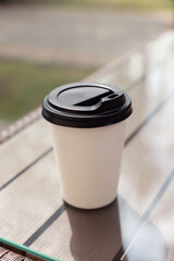 Paper takeaway cup on glass table outdoors. Coffee to go