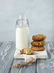 Stack of oatmeal cookies with cranberry, cashew nuts and white chocolate on a white wooden cutting board near glass bottle of milk. Grey wooden table, grey wall on the background. Rustic style