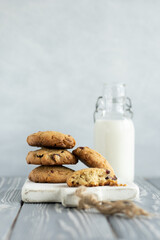 Stack of oatmeal cookies with cranberry, cashew nuts and white chocolate on a white wooden cutting board. Glass bottle of milk on the background. Grey wooden table, rustic style